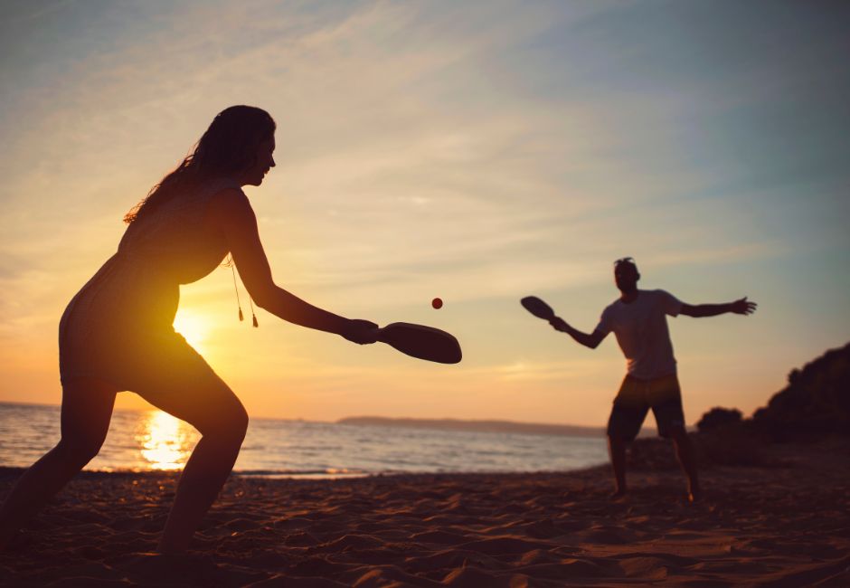 Couple playing paddle ball on the beach at sunset